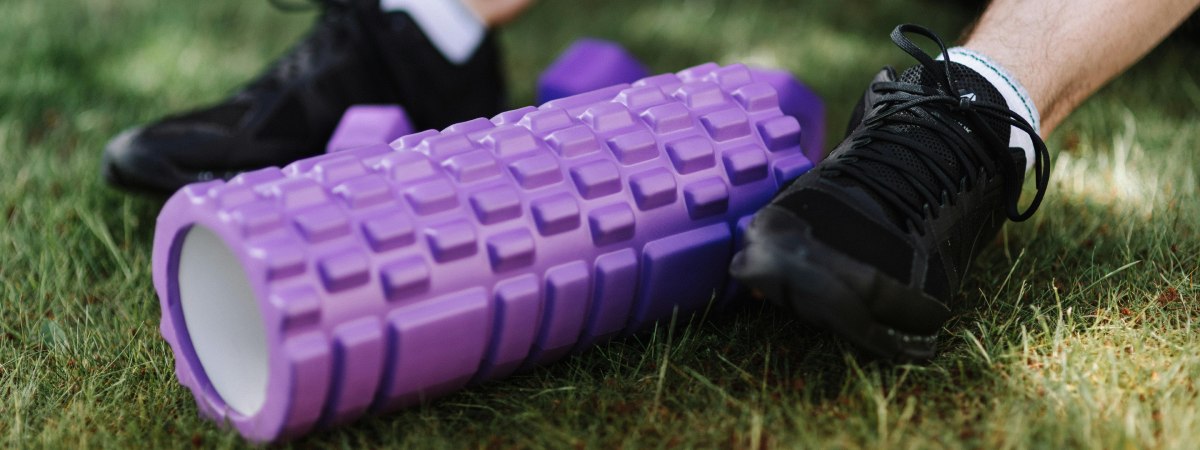 A pair of feet in black trainers either side of a purple textured roller for self massage